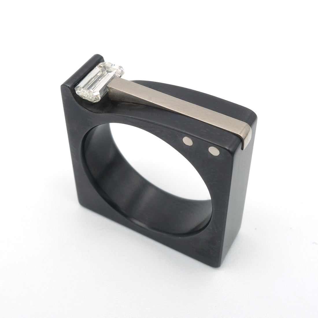 Strakke blokvormige ring van zwart zirkonium met een witgouden inlay, gezet met een emerald geslepen diamant op een witte achtergrond.