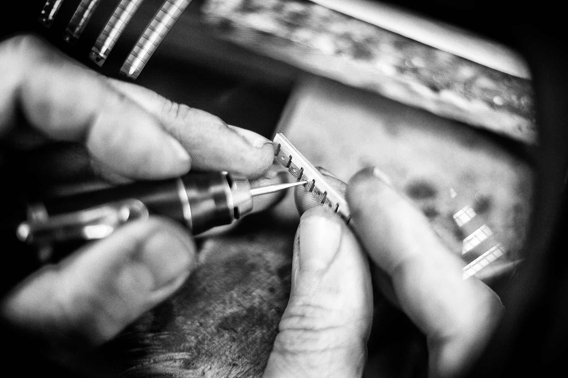 Wouter Dijkman schuurt een sieraadonderdeel af – zwart-witfoto van het fijne slijpwerk in het atelier.

