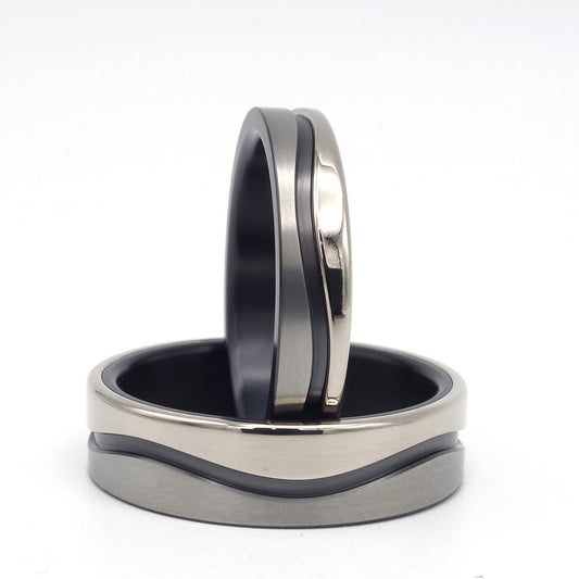 Twee trouwringen met golvend ontwerp van zwart zirkonium en 14 karaat witgoud, in 4,5 mm en 7 mm breedte, samen gepresenteerd.

