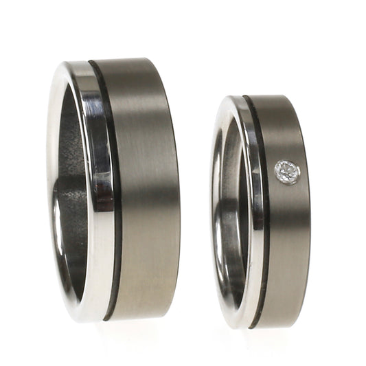 Twee trouwringen van edelstaal en zirkonium; één met diamant, één zonder, samen gepresenteerd als trouwset.